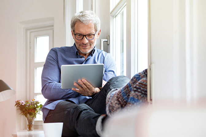 Mann sitzt an Fenster mit Tablet in der Hand