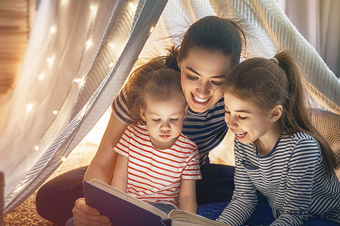Mutter liest zwei Töchtern zuhause etwas aus Buch vor